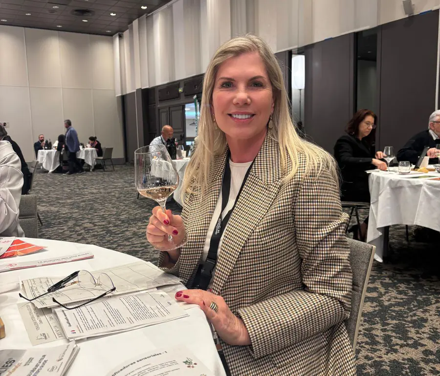 Regina Vanderlinde à mesa de uma degustação técnica, com a taça na mão e as fichas de análise sensorial